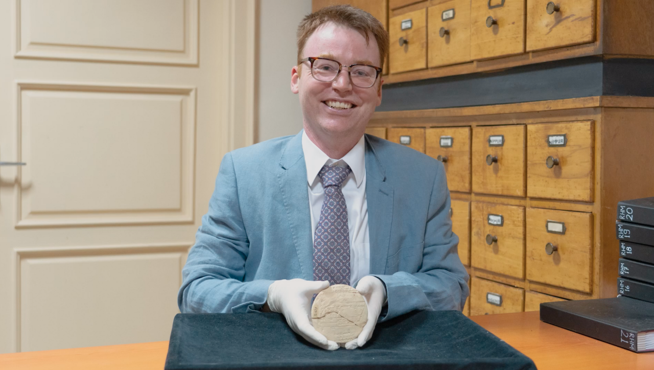 Dr Mansfield sits in a museum room proudly holding tablet Si.427 in white-gloved hands